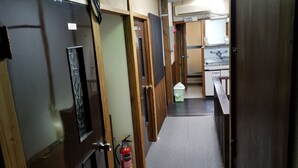 A narrow hallway with wooden doors, a fire extinguisher, and a tiled floor leading to a kitchen area. - Ryokan Katsutaro (Tokyo)