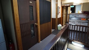 A hotel room with a wooden door, a small window, a metal railing, and a kitchenette area with a sink and cabinets. - Ryokan Katsutaro (Tokyo)