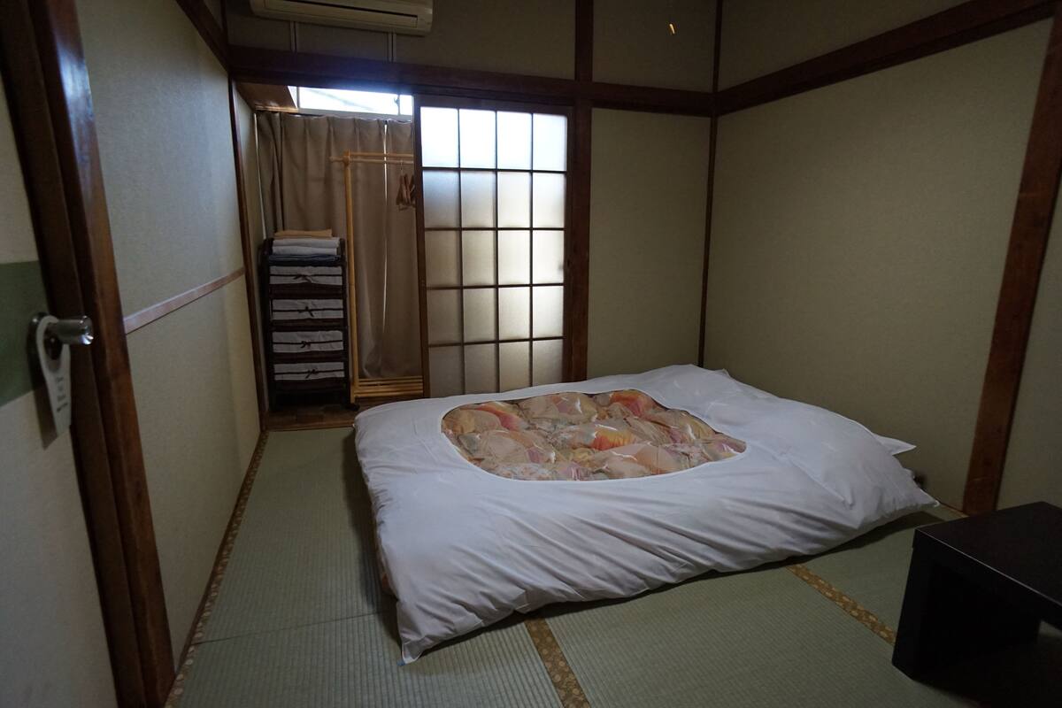 A traditional Japanese room with tatami flooring, a futon bed, a sliding door, and a small black table.