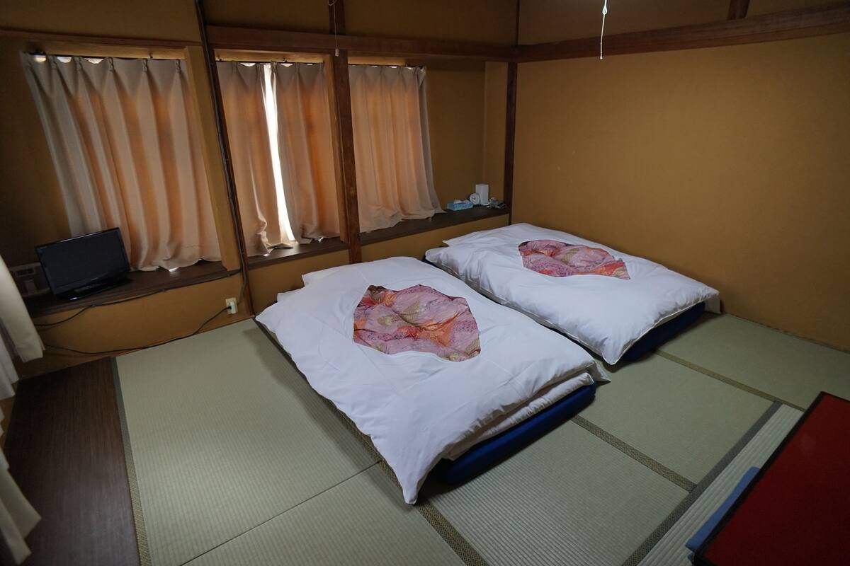 A room with two beds, a desk with a laptop, and a window with curtains.