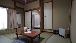 A traditional Japanese room with tatami flooring, a wooden table with a cushion, a heater, and a sliding door leading to a bed. - Ryokan Katsutaro (Tokyo)