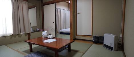 Una habitación japonesa tradicional con suelo de tatami, una mesa de madera con cojín, un calentador y una puerta corredera que da a la cama.