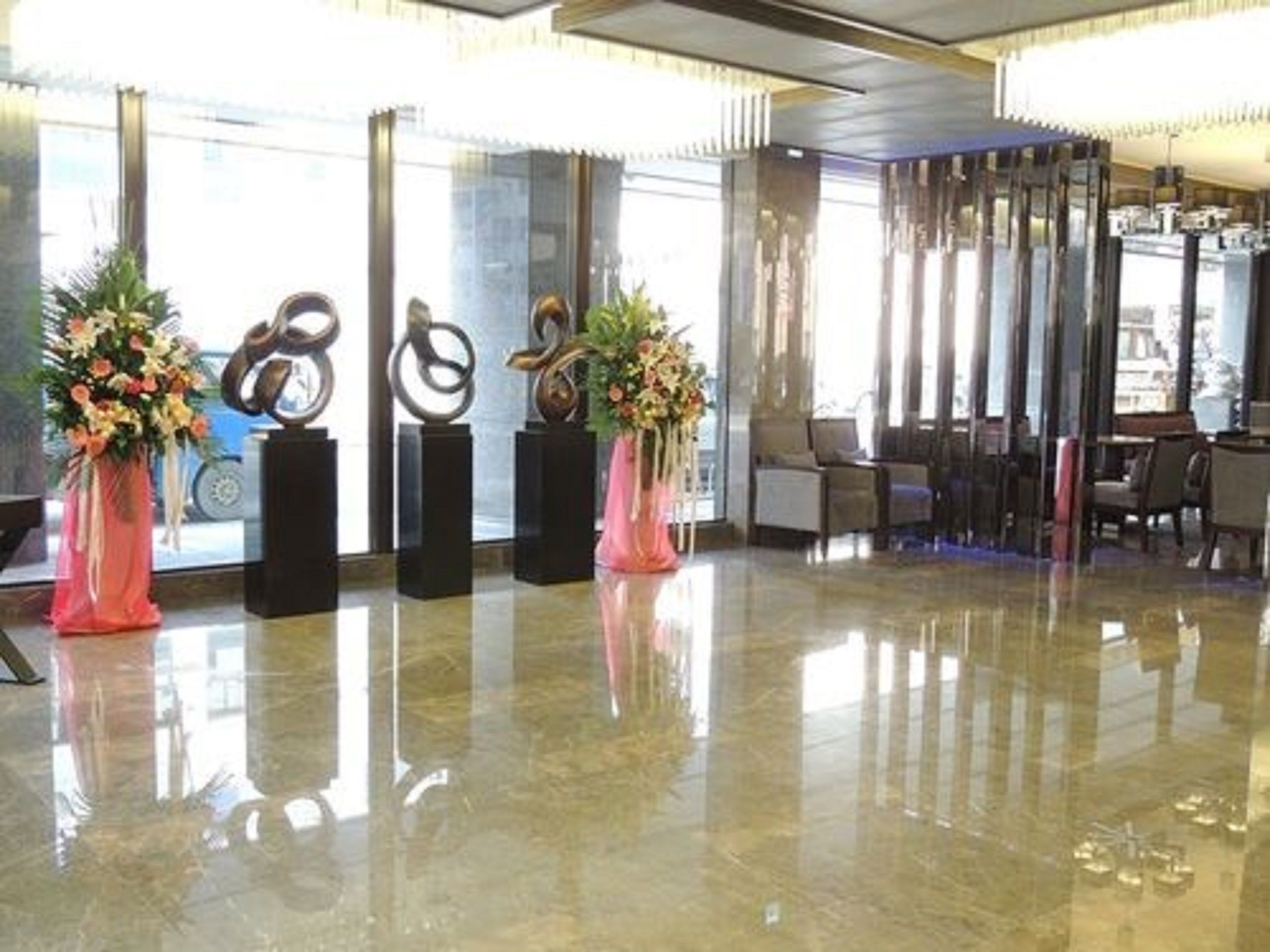 Un vestíbulo con piso pulido, ventanas amplias y jarrones decorativos con flores.