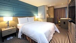 A hotel room with a large bed, bedside tables with lamps, a small desk, a chair, a minibar, and a view of the city. - International Citizen Hotel (Kaohsiung)