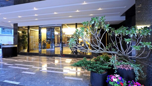 A hotel entrance with a glass facade, potted plants, and a tiled floor. - International Citizen Hotel (Kaohsiung)