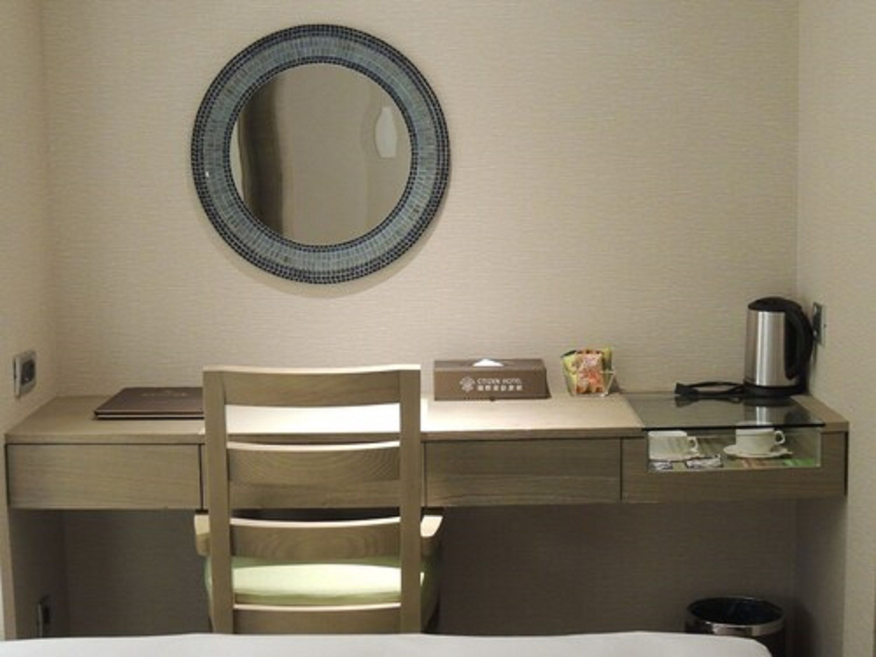 A hotel room with a wooden desk, a chair, a coffee maker, a box, and a cup.