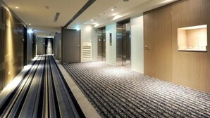 A hotel corridor with a patterned carpet, wooden panel walls, and a modern elevator. - International Citizen Hotel (Kaohsiung)