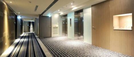 A hotel corridor with a patterned carpet, wooden panel walls, and a modern elevator.