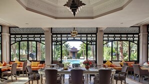 Comedor con vista a una piscina y palmeras, que cuenta con un techo alto con diseños intrincados y un candelabro.