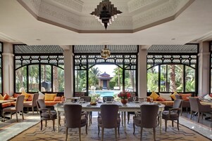 Comedor con vista a una piscina y palmeras, que cuenta con un techo alto con diseños intrincados y un candelabro.