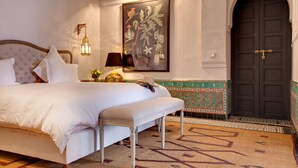 Una cama bien hecha con almohadas, una lámpara de noche y una obra de arte colgada en la pared.
