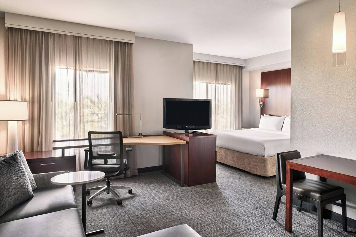 A hotel room with a bed, a desk with a TV, a sofa, and a chair.