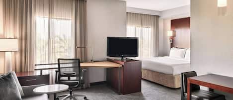 A hotel room with a bed, a desk with a TV, a sofa, and a chair.