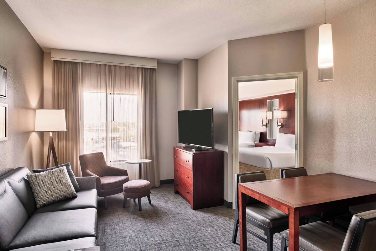 A hotel room with a sofa, armchair, ottoman, TV stand, and a dining table.