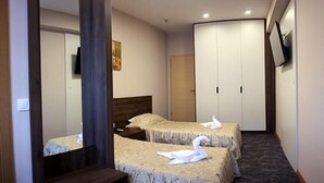 A hotel room with two beds, a large mirror, a wardrobe, and a television on the wall. - Ambasador (Skopje)