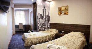 A hotel room with two beds, a cityscape mural, a painting, and a desk with a chair. - Ambasador (Skopje)