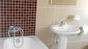 A bathroom with a bathtub, a sink, and a mirror. - Ambasador (Skopje)