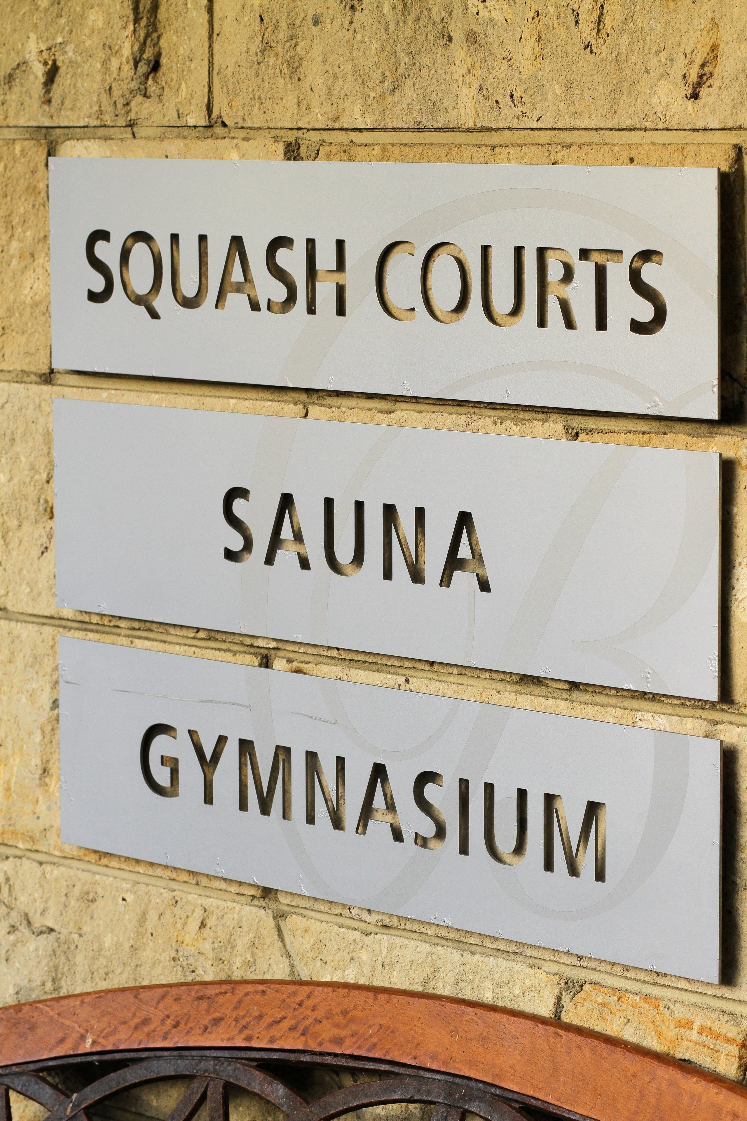 Un letrero con tres secciones que indican 'Canchas de Squash', 'Sauna' y 'Gimnasio'.
