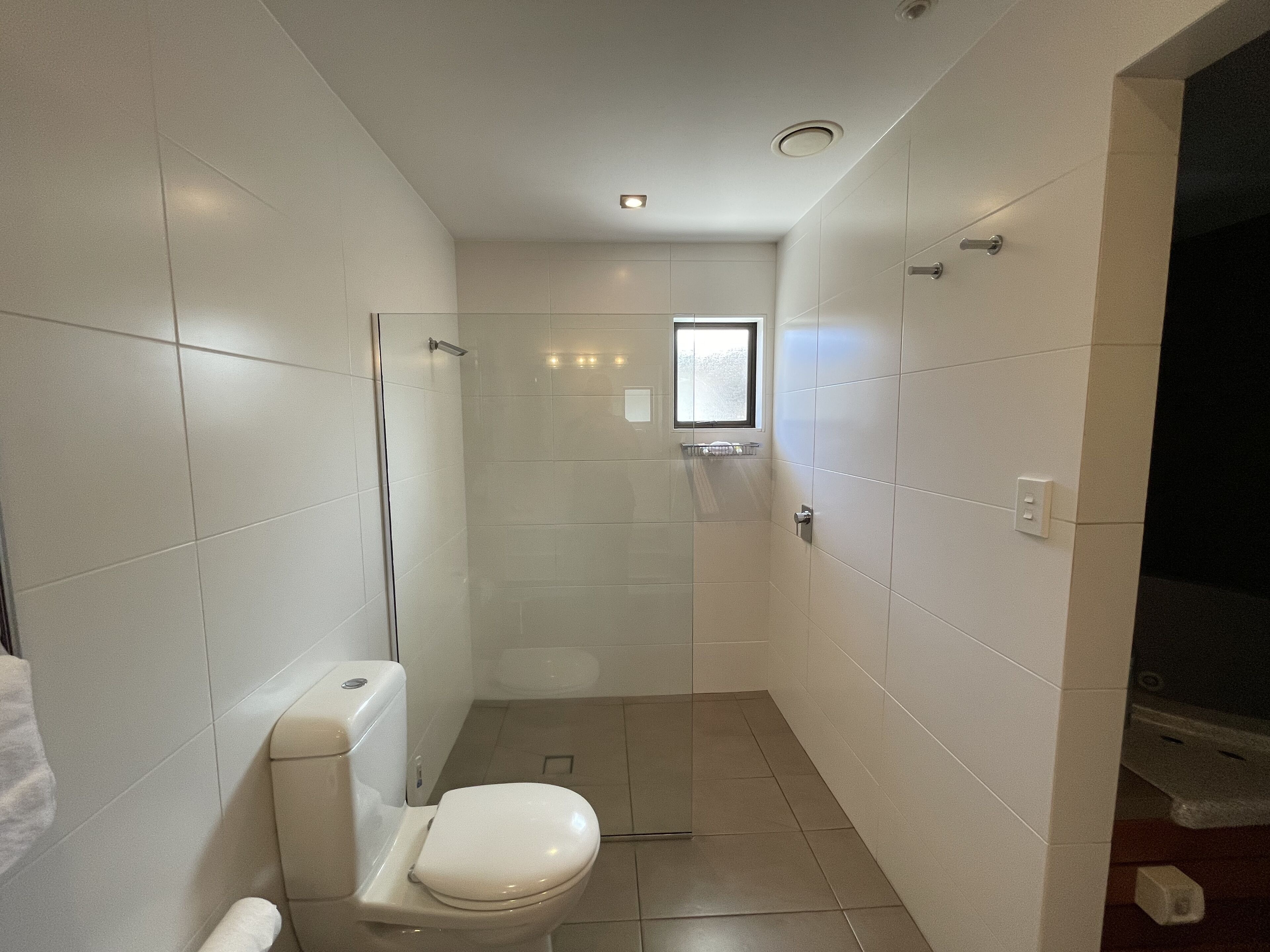 A small, modern bathroom with a toilet, a glass shower enclosure, and a window.