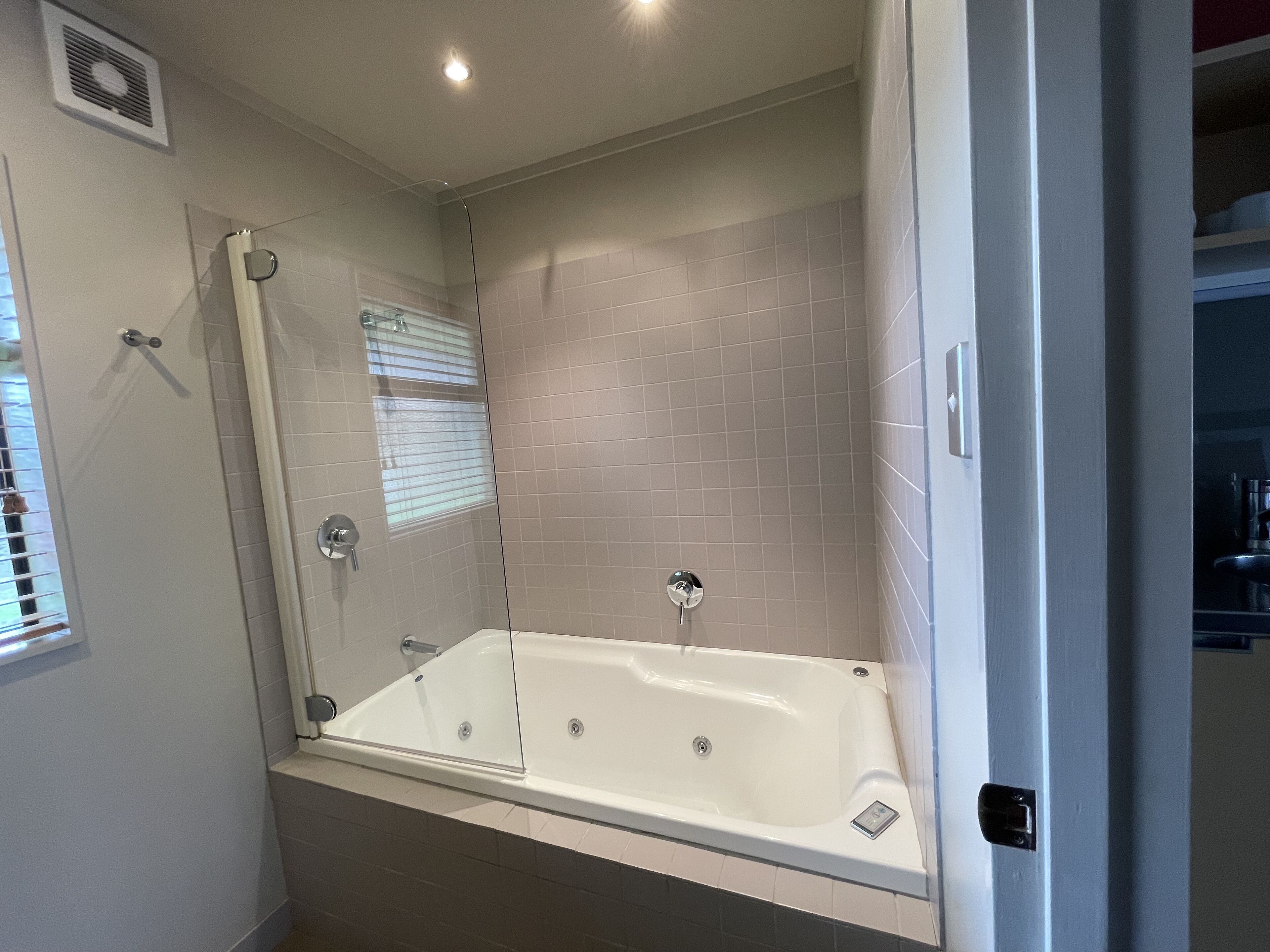 A bathroom with a walk-in shower, a bathtub, and a window with blinds.