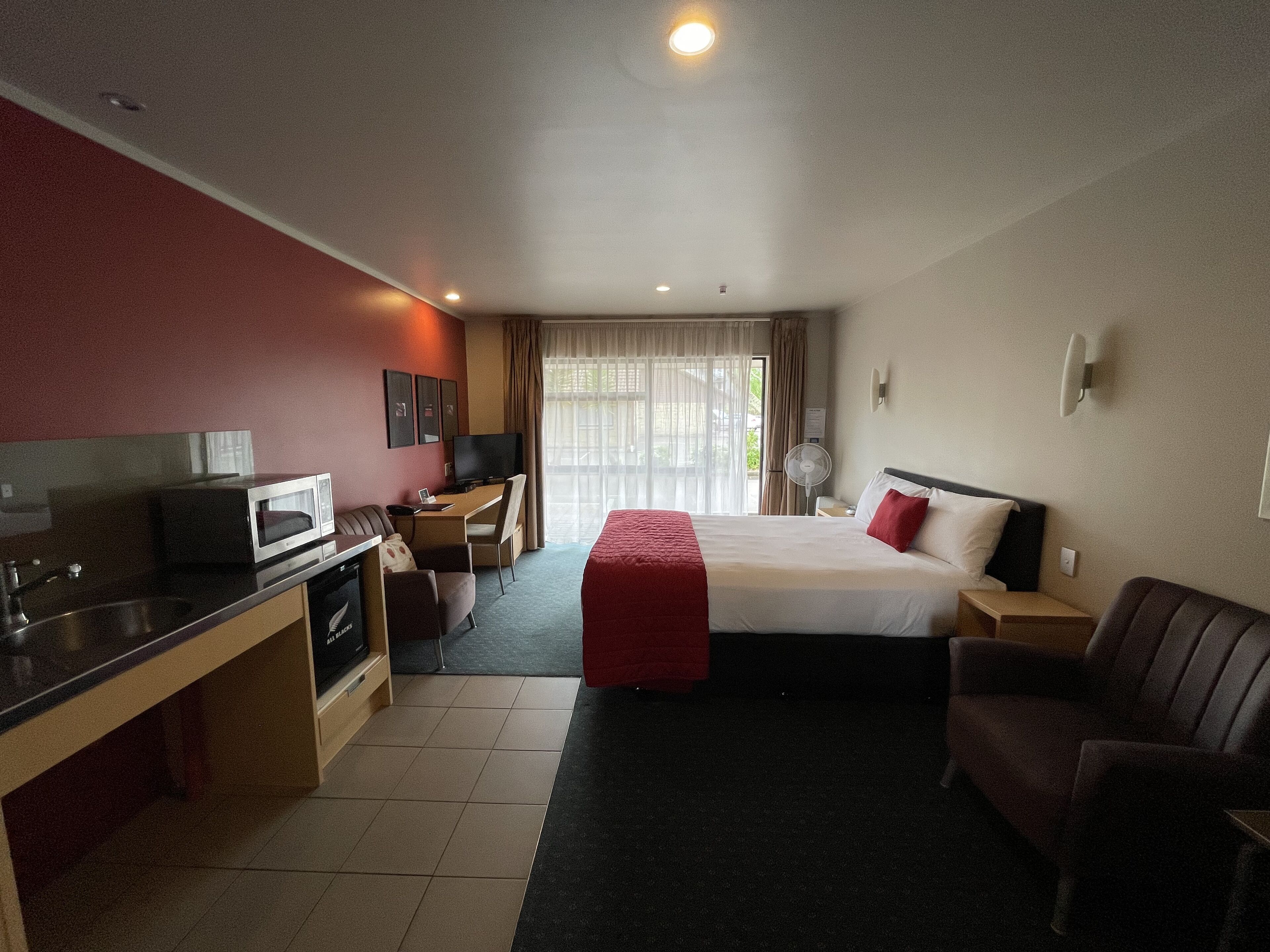 Habitació d'hotel amb un llit, una taula amb ordinador, microones, una cadira i un televisor.