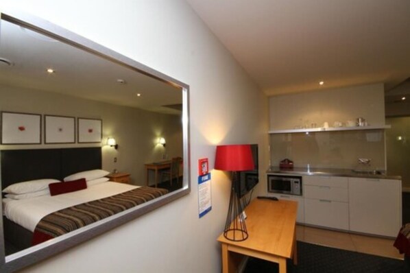 A hotel room with a large bed, a desk, a kitchenette, and a mirror reflecting the room. - Bentleys Motor Inn (Palmerston North)