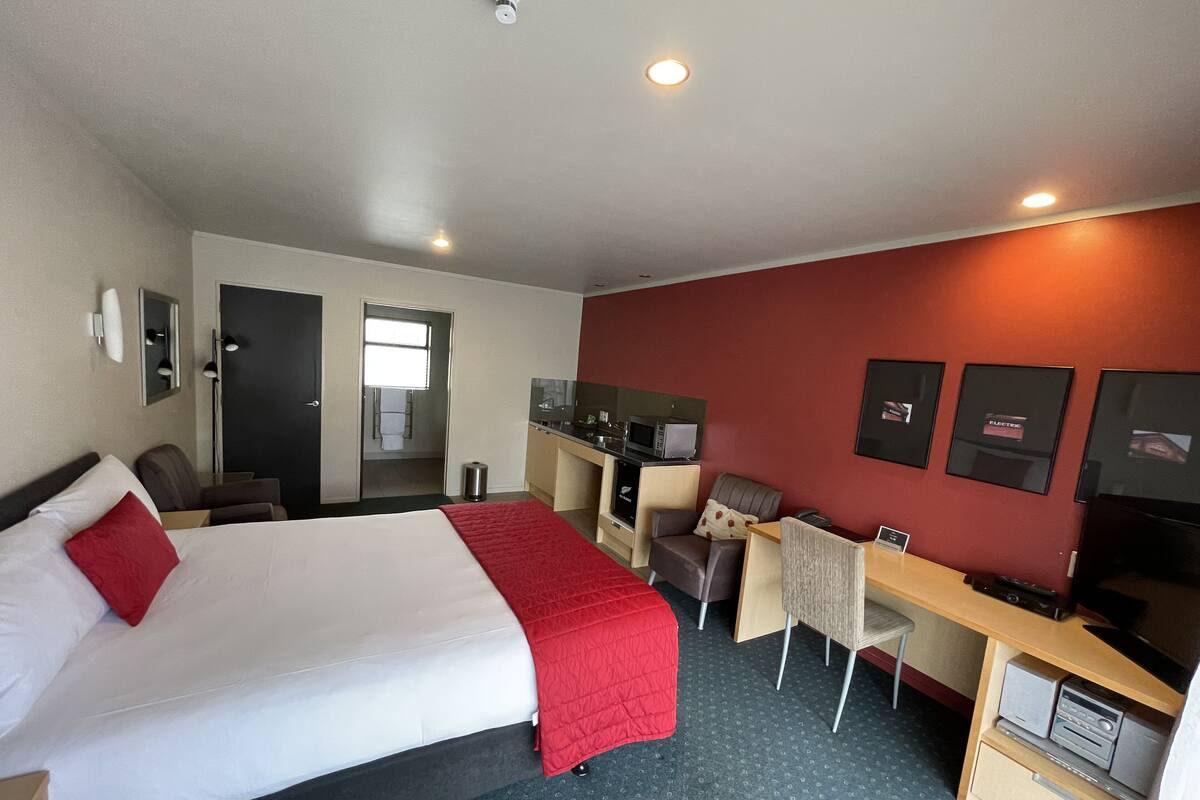 Hotellihuone, jossa on sänky, työpöytä, tuoli, televisio ja pieni keittonurkkaus.
