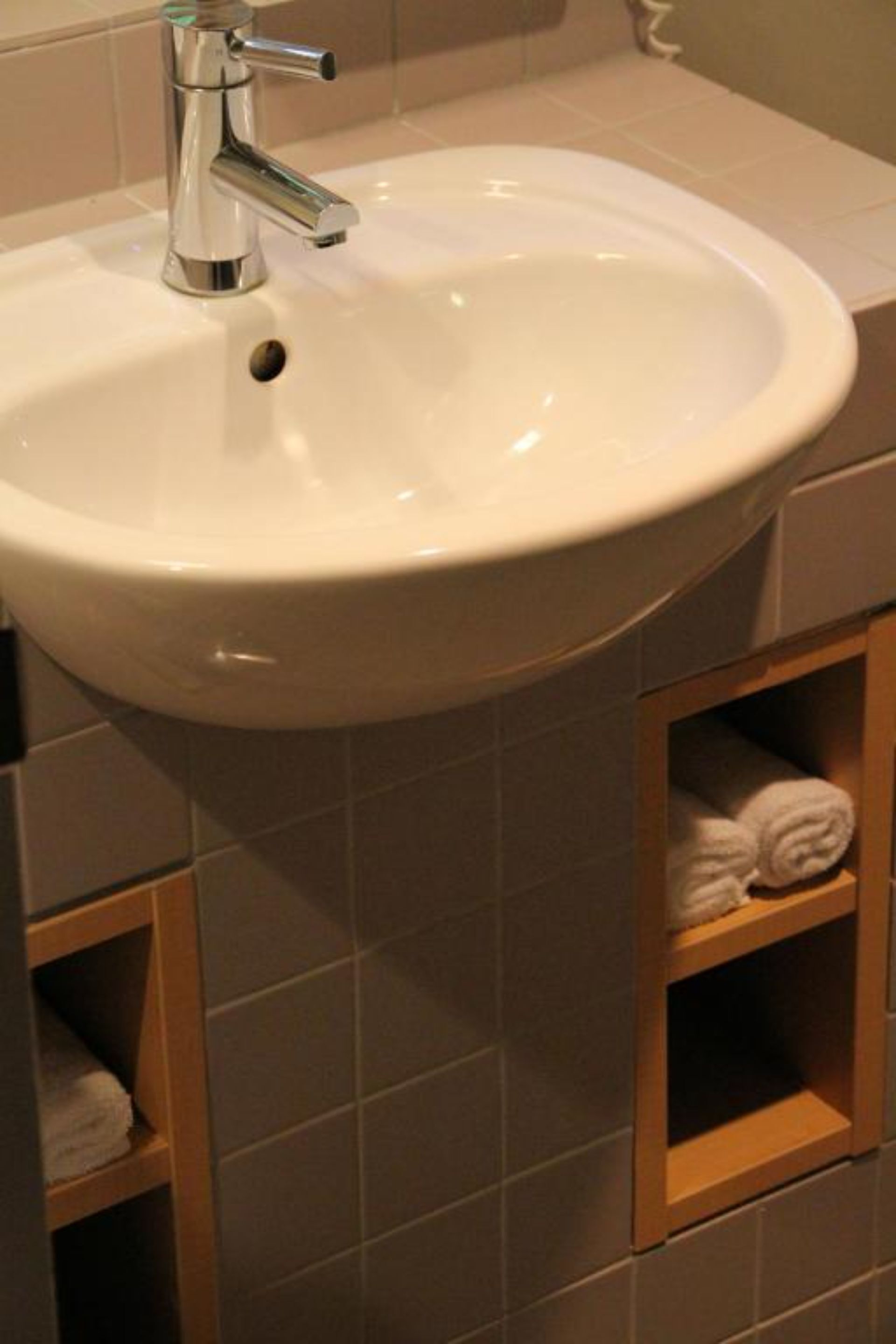 Un baño con lavamanos blanco, grifo cromado y repisas de madera para toallas.
