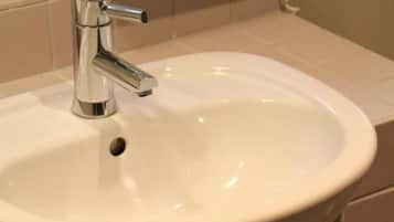 Un baño con lavamanos blanco, grifo cromado y repisas de madera para toallas.