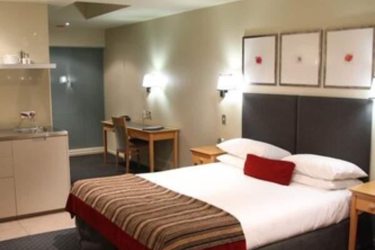 Hotellihuone, jossa on sänky, työpöytä, tuoli, pieni keittonurkkaus ja kylpyhuone.