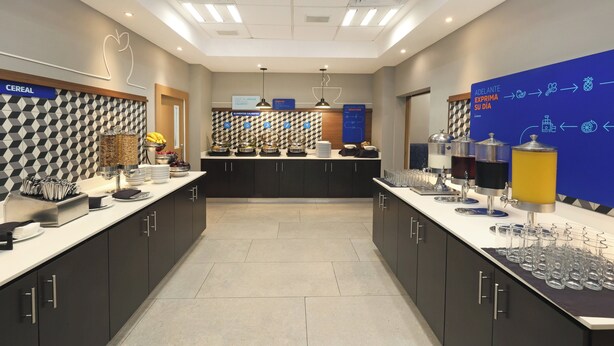 A modern hotel kitchen with a breakfast bar, various food stations, and a blue informational wall. - Holiday Inn Express Veracruz Boca Del Rio by IHG (Boca del Río)