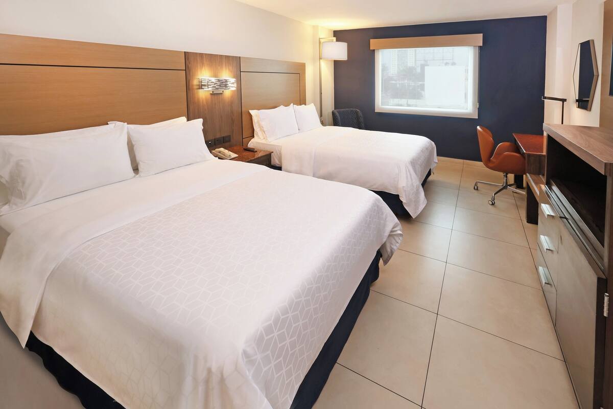 A hotel room with two beds, a desk, a chair, a TV, and a window with a view.