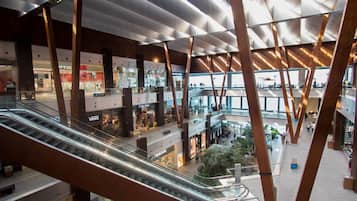Un centro comercial de varios niveles con escaleras mecánicas, barandillas de vidrio y diversas tiendas.