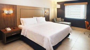 A hotel room with a large bed, a bedside table with a phone, a seating area with a chair, and a window with a view of buildings. - Holiday Inn Express Veracruz Boca Del Rio by IHG (Boca del Río)