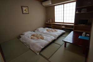 A room with two beds, a wooden desk, a window with a grid pattern, and a shelf with various items. - Annex Katsutaro Ryokan (Tokyo)