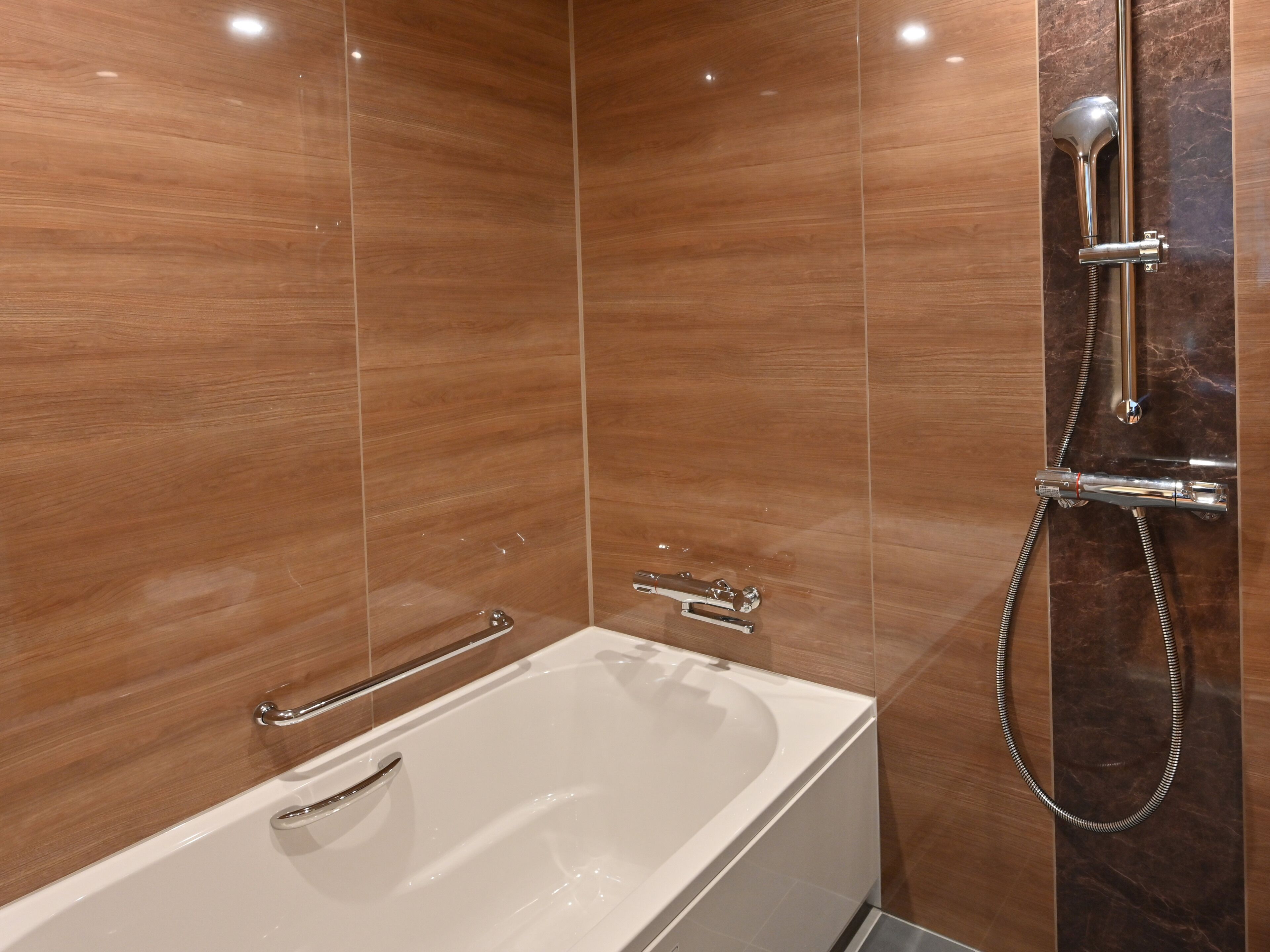 A modern bathroom with a white bathtub, a handheld showerhead, and a wall-mounted faucet.