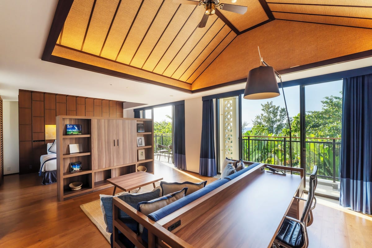 A modern interior with a long wooden dining table, a built-in bookshelf, and a ceiling fan.