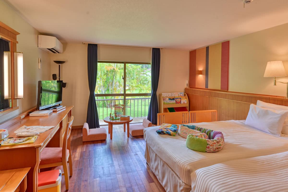 A hotel room with a bed, a desk, a chair, a television, a window with curtains, and a balcony with a view of greenery.