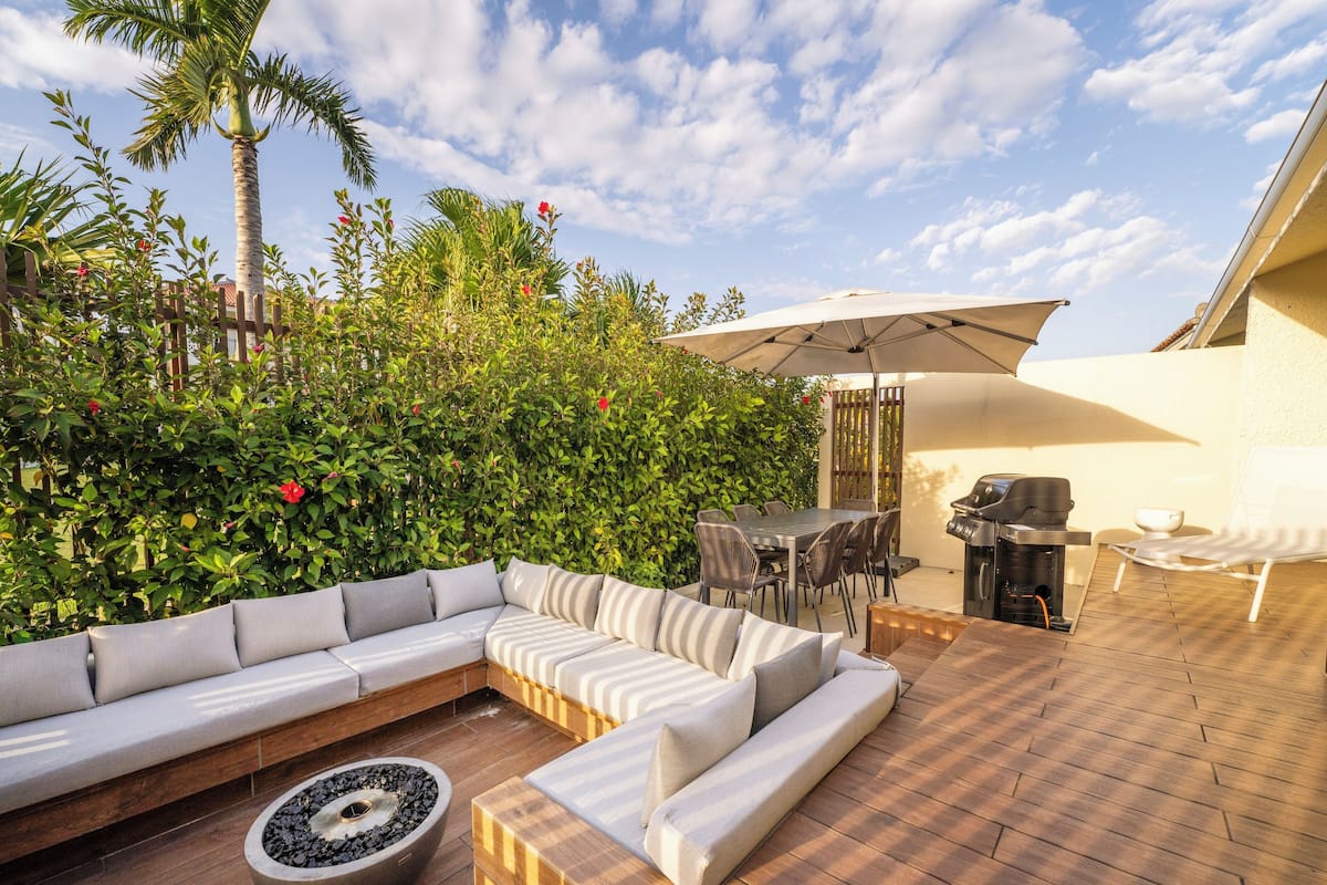 A covered outdoor seating area with a sofa, dining table, and grill.