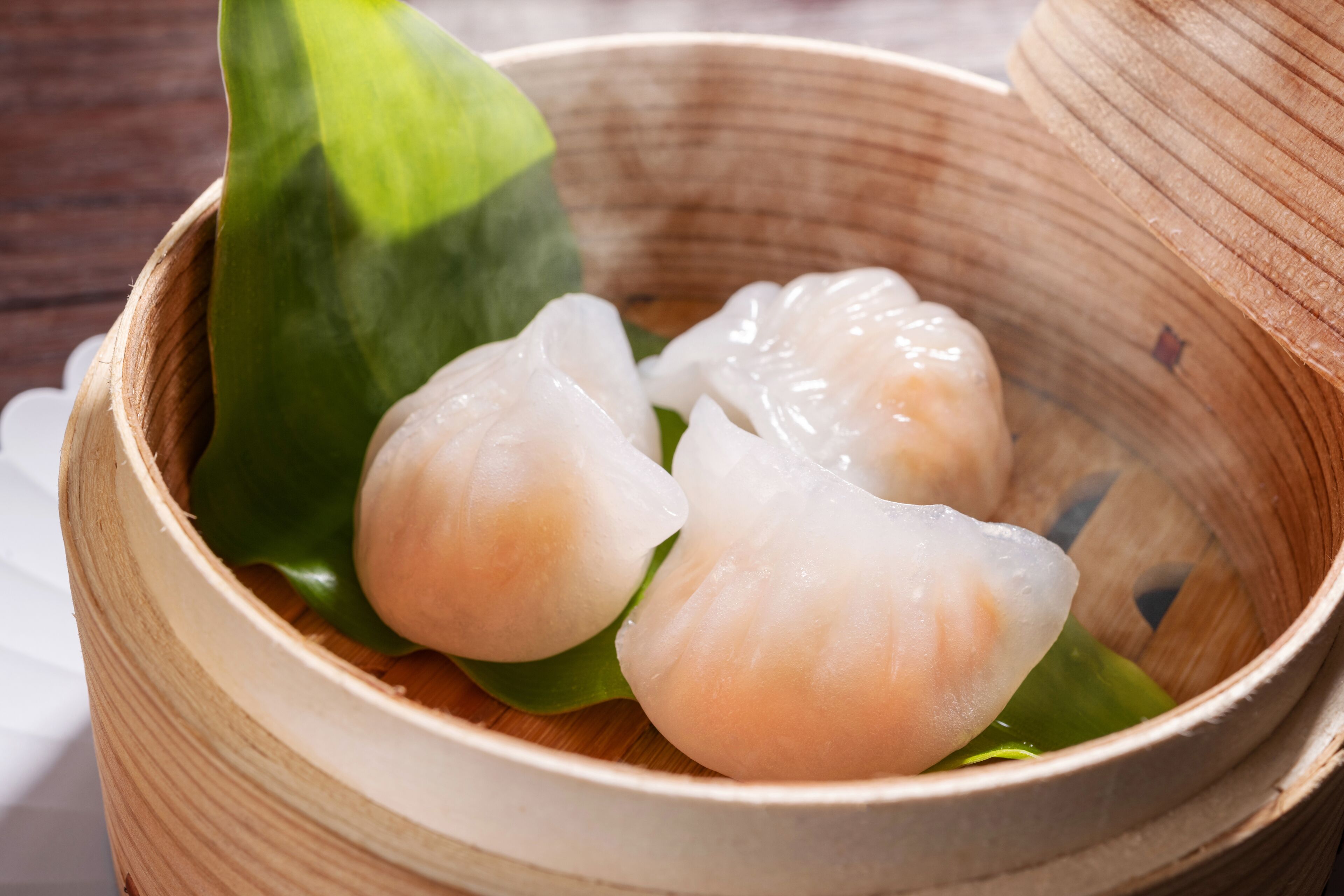 A wooden bowl containing three translucent dumplings on a green leaf.