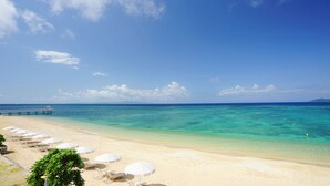 A beach with white umbrellas and lounge chairs, a pier extending into the water, and clear turquoise sea. - Fusaki Beach Resort Hotel & Villas (Ishigaki)