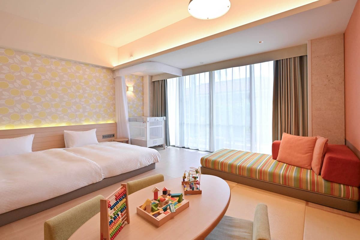 A modern hotel room with a large bed, a sofa, a dining table, and a play area.