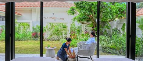 Una habitación con dos camas, una mesa de comedor y vistas a un jardín donde alguien cuida las plantas.