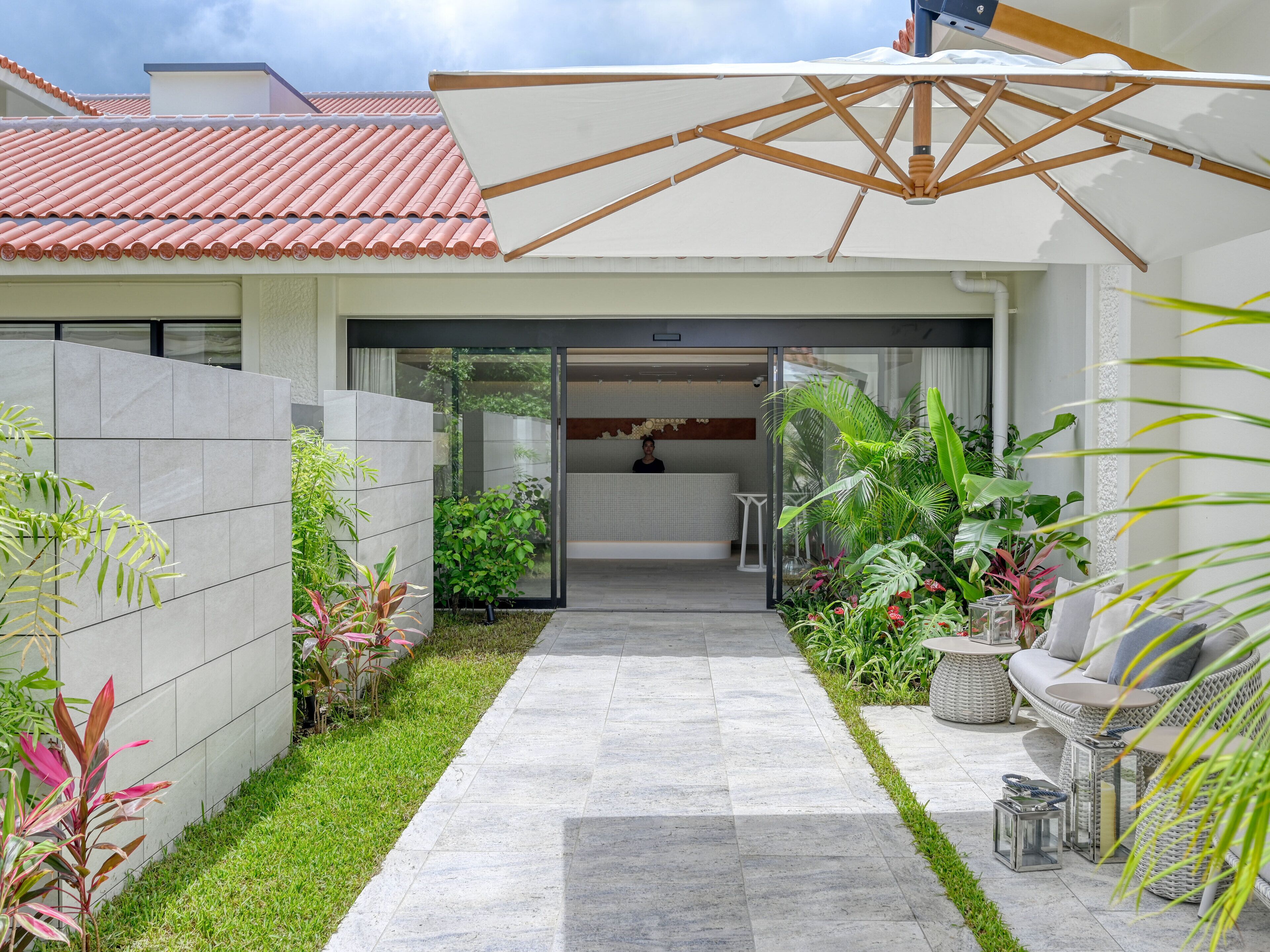 Una casa moderna con techo de tejas, un sendero de concreto y una zona de recepción con una persona sentada.