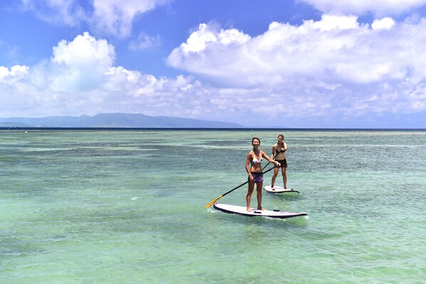 Two people paddleboarding on a clear blue sea with mountains in the background.