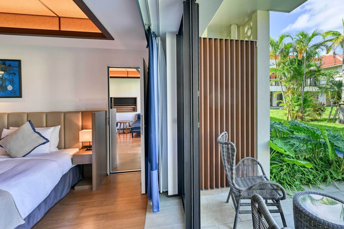 A modern hotel room with a bed, a desk, and a balcony with wicker chairs and a glass table.