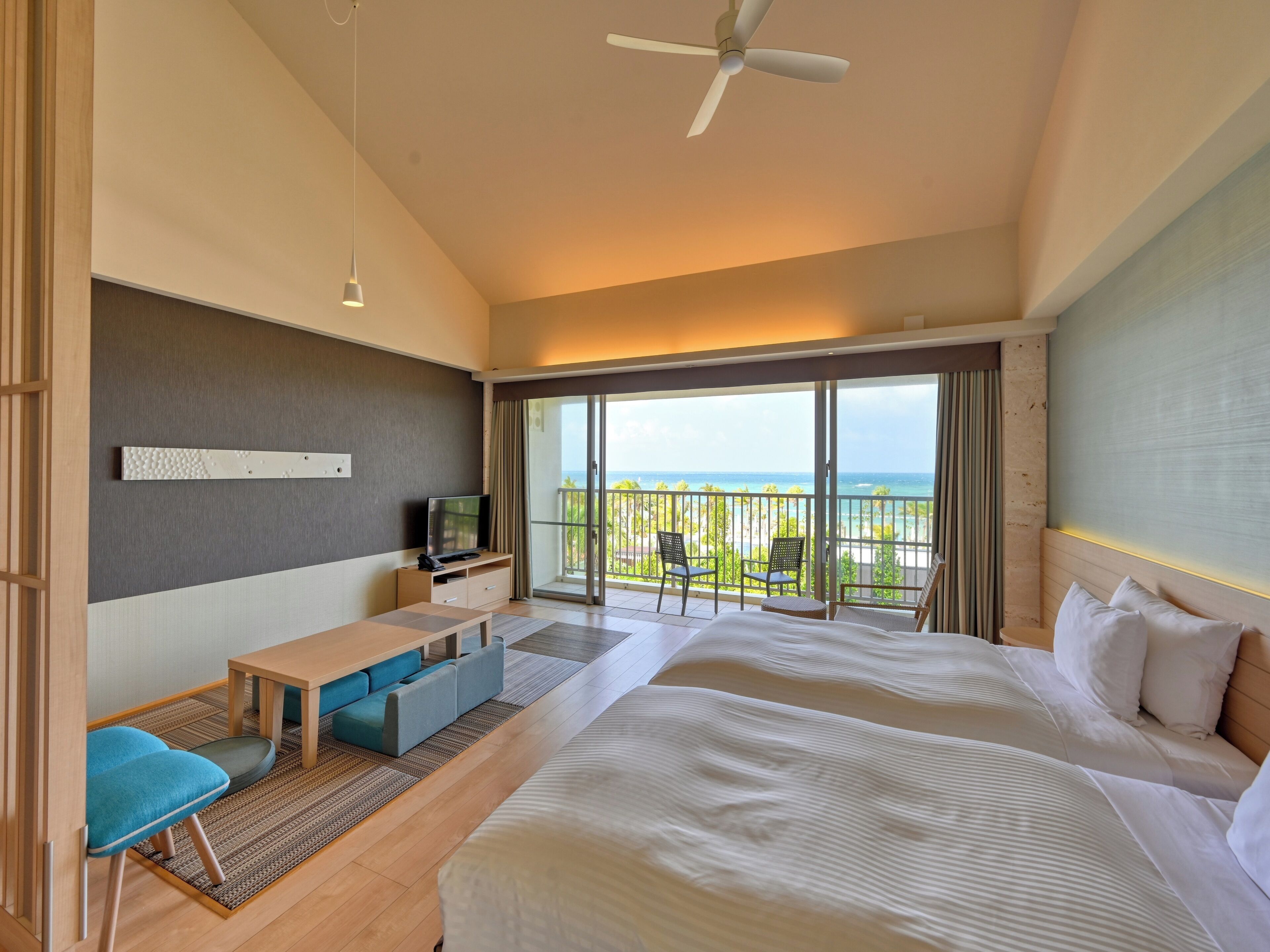 A hotel room with a balcony, a TV, a desk, and two beds.