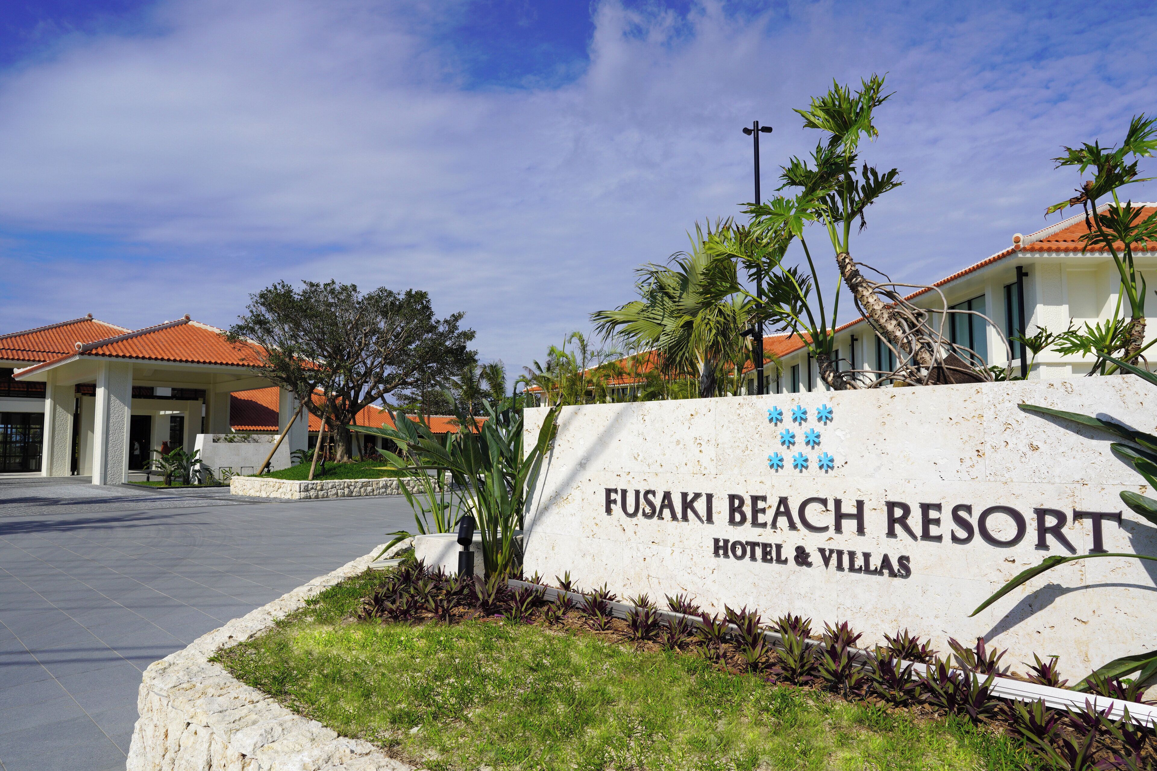 Señal del Hotel & Villas Fusaki Beach Resort, con cielo despejado y palmeras.