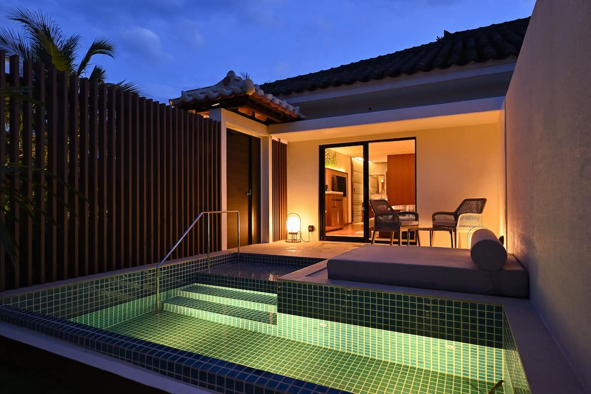 A modern house with a swimming pool, a patio with chairs, and a sliding door leading to the interior.