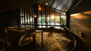 A hot tub with a view of greenery outside, surrounded by a dark interior with wooden walls and a glass partition. - Fusaki Beach Resort Hotel & Villas (Ishigaki)
